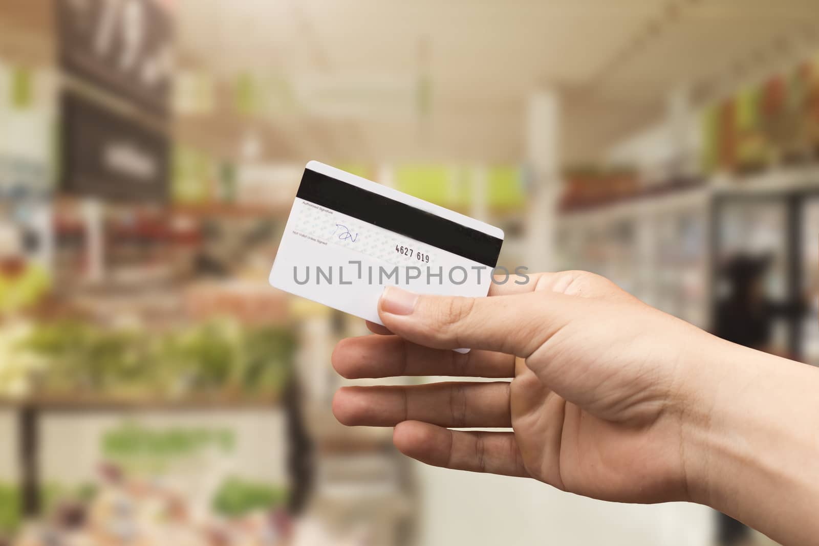 female hand holding credit card with blurry supermarket background by Gobba17