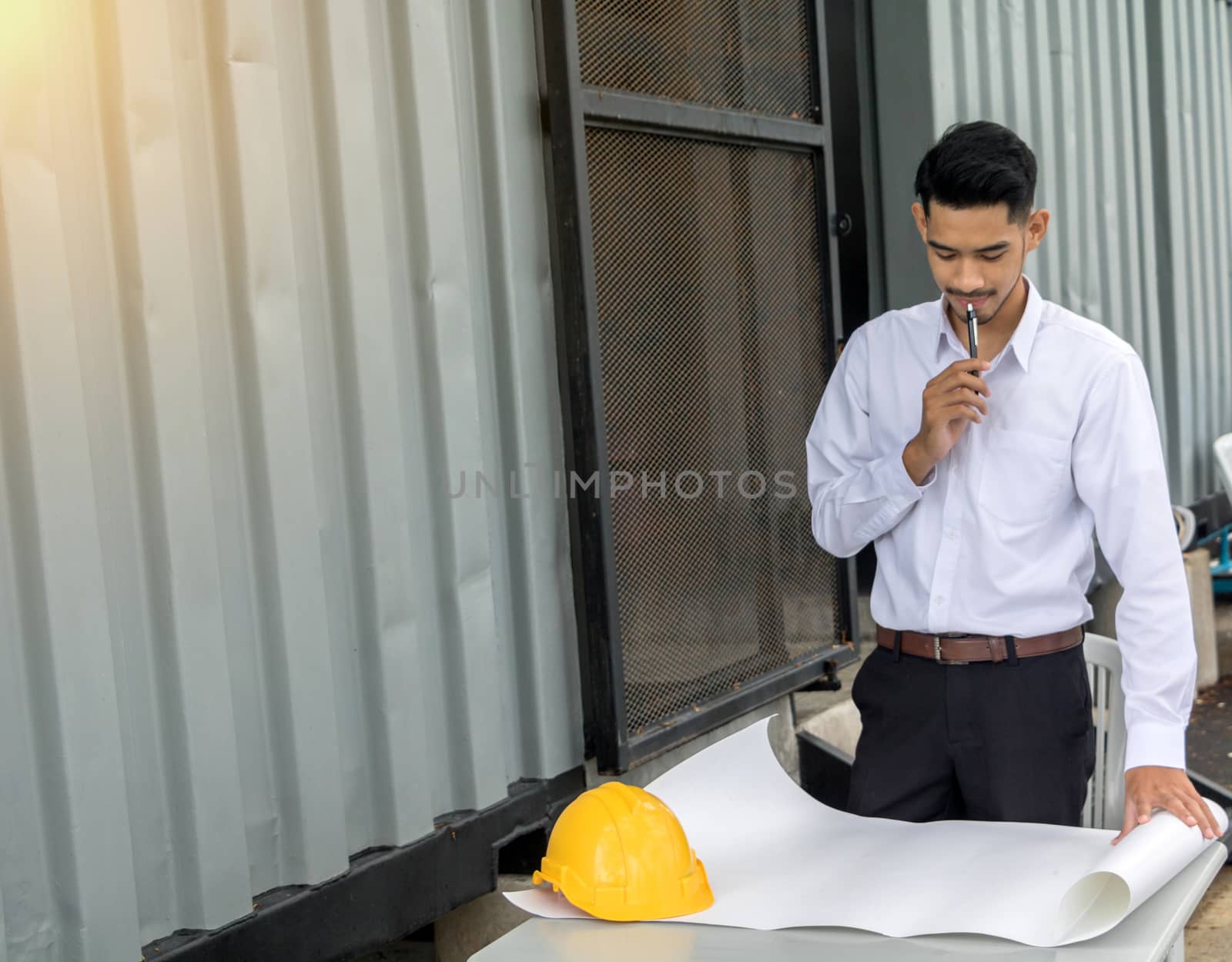Young Asia man engineer wearing safety helmet in white shirt checking construction site building.