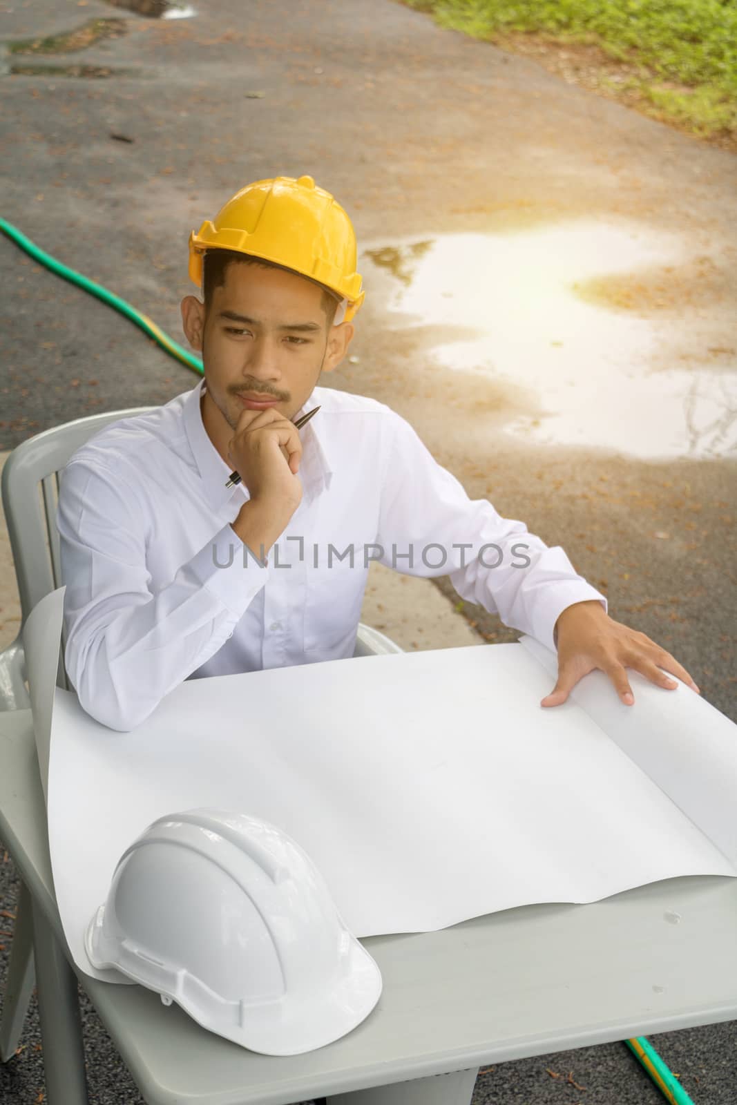 Young Asia man engineer wearing safety yellow helmet in white shirt checking construction site building.