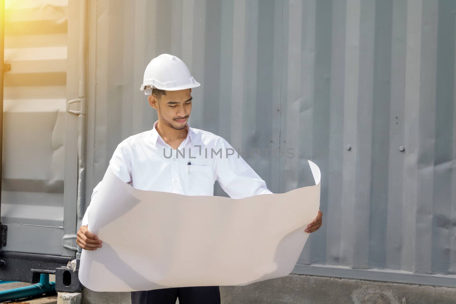 Young Asia man engineer wearing safety white helmet in white shirt checking construction site building.