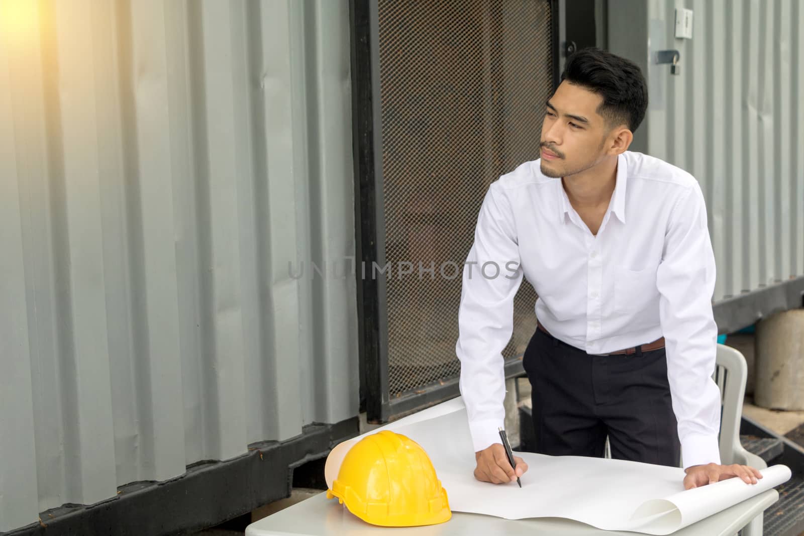 Young Asia man engineer wearing safety helmet in white shirt checking construction site building.