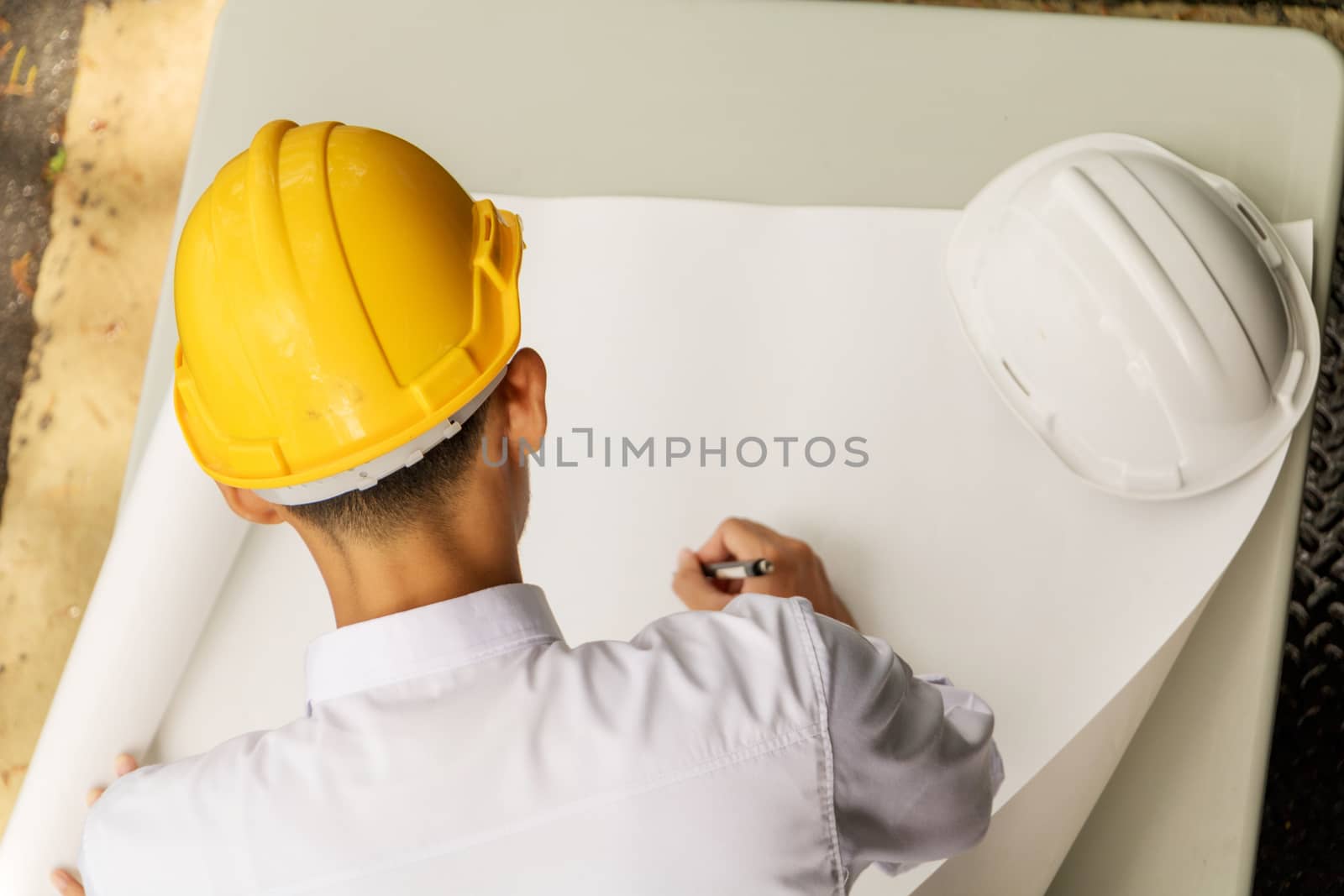 Young Asia man engineer wearing safety yellow helmet in white shirt checking construction site building.