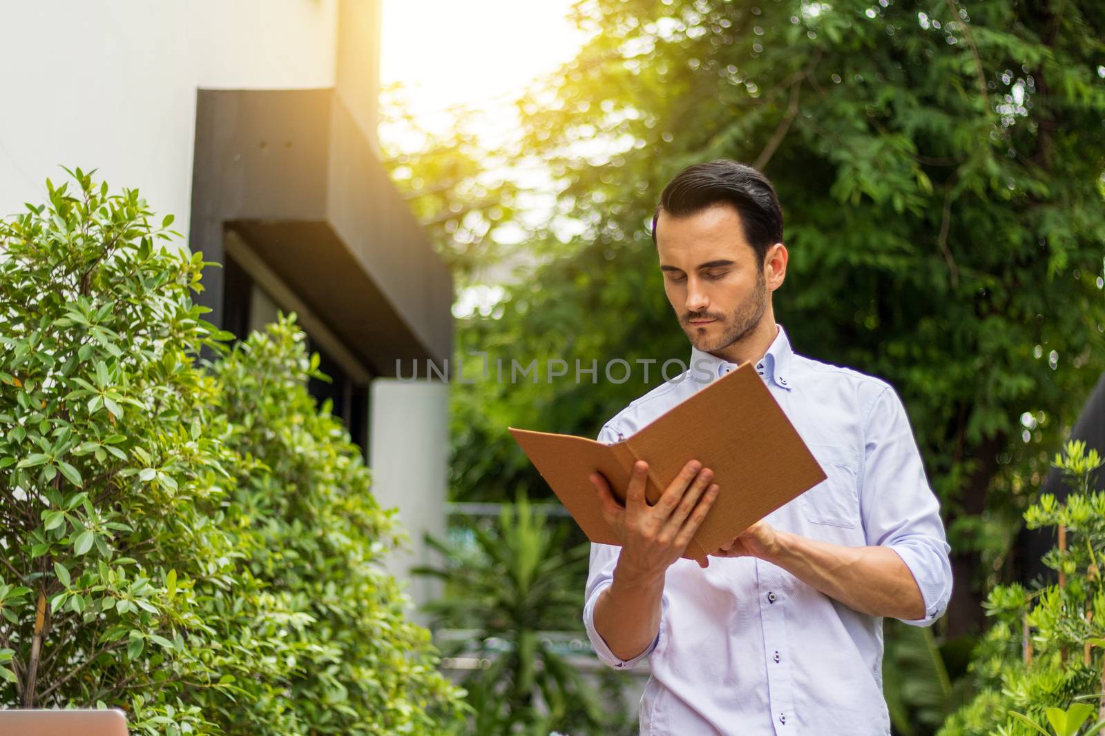 A young man reading a book in the garden. There's a notebook on the table to use information and work.Young man working in the garden.