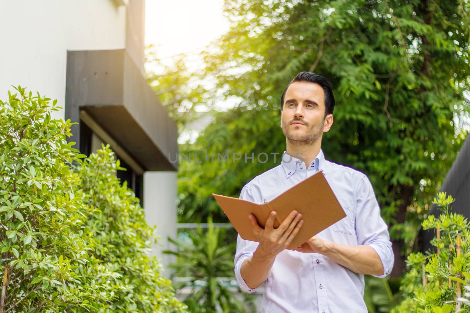 A young man stands reading a book in the garden. Young man working in the garden.