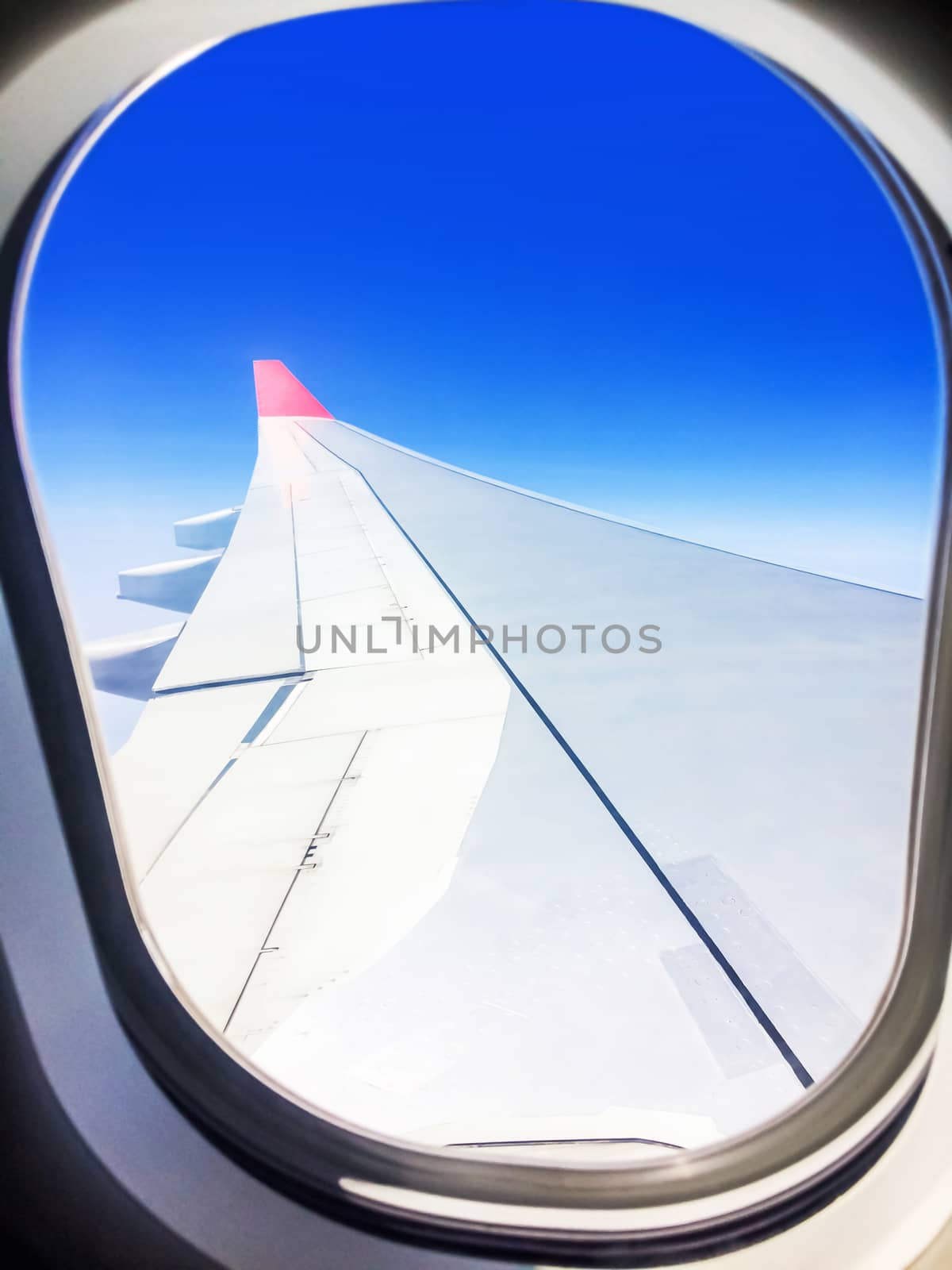 View of a commercial aeroplane from window where you can see the wing which flies above the clouds at height 35,000 feet.