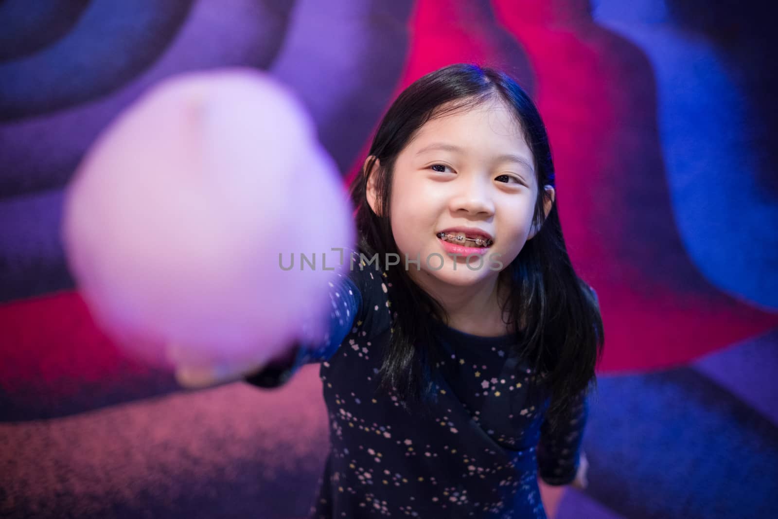 Little Asian girl holding cotton candy in her hand with smiling face.