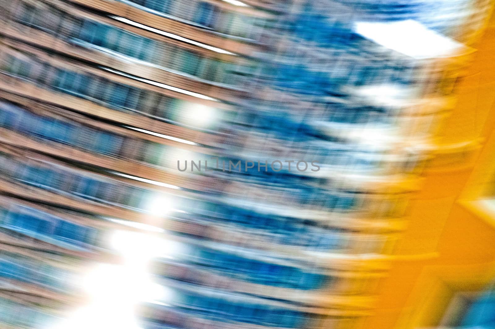 A blue and orange abstract photographic view of buildings in movement in the city, with a grain reticulation texture effect
