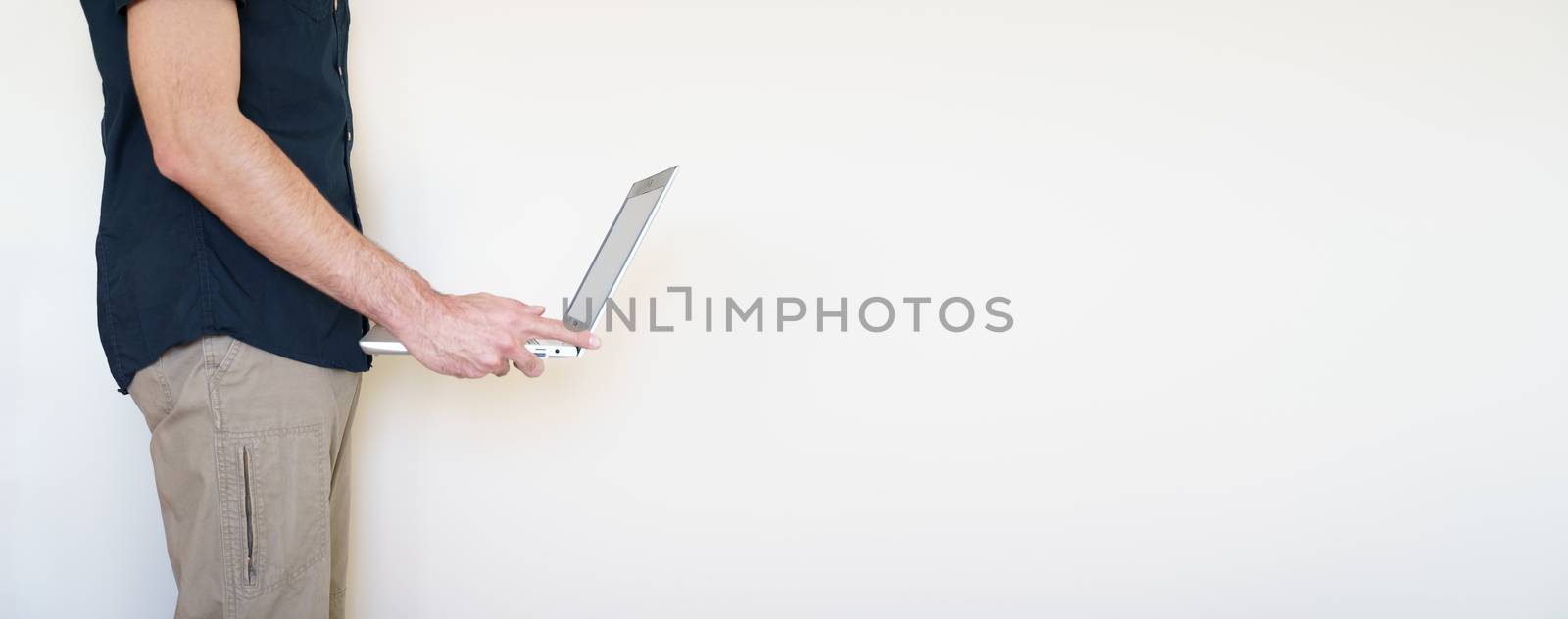 Male digital nomad hand holding a laptop over a light beige color background. Copy space available