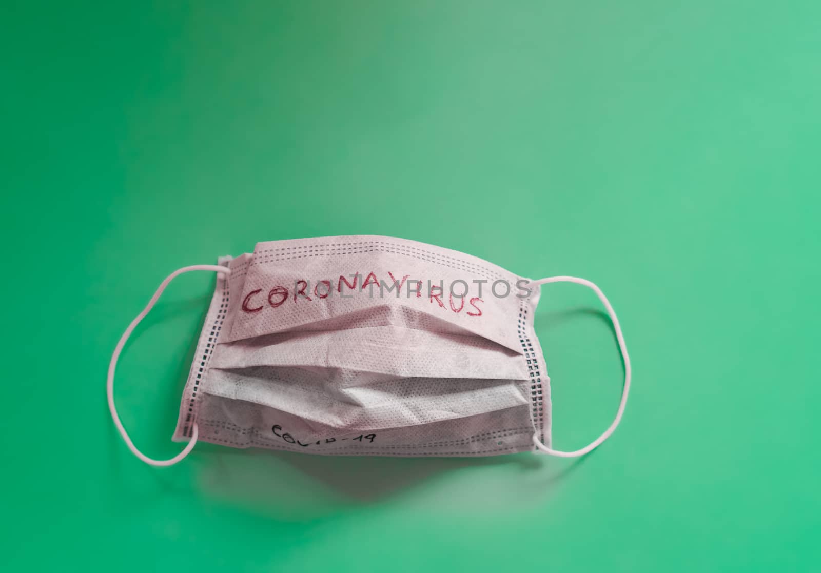 White medical mask with coronavirus word on it isolated on green background. Face mask protection against pollution, virus, flu and coronavirus. Health care and surgical concept.