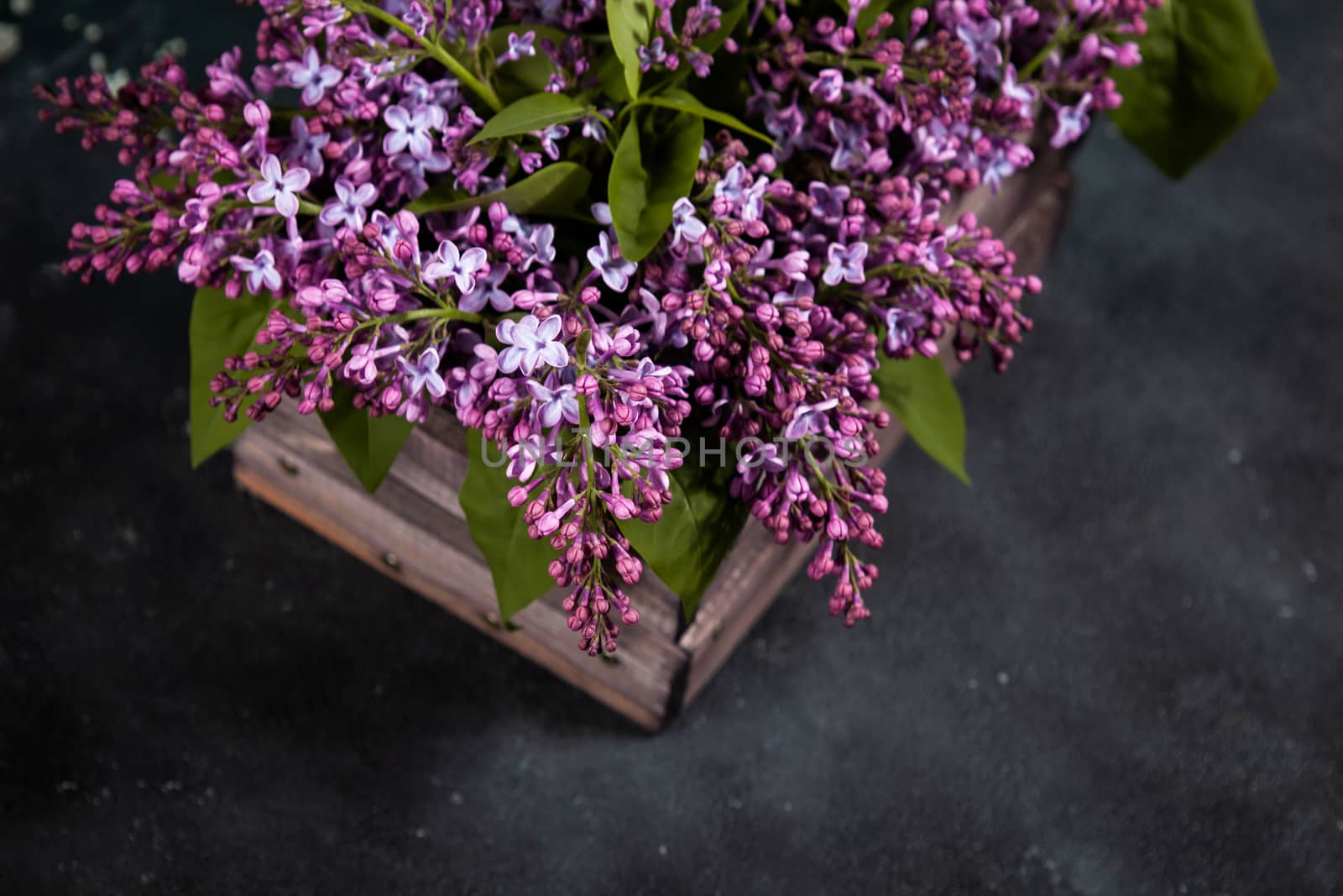 Purple lilac flowers bouquet on wooden box on black concrete background. Stylish floral greeting card. Happy mothers day.