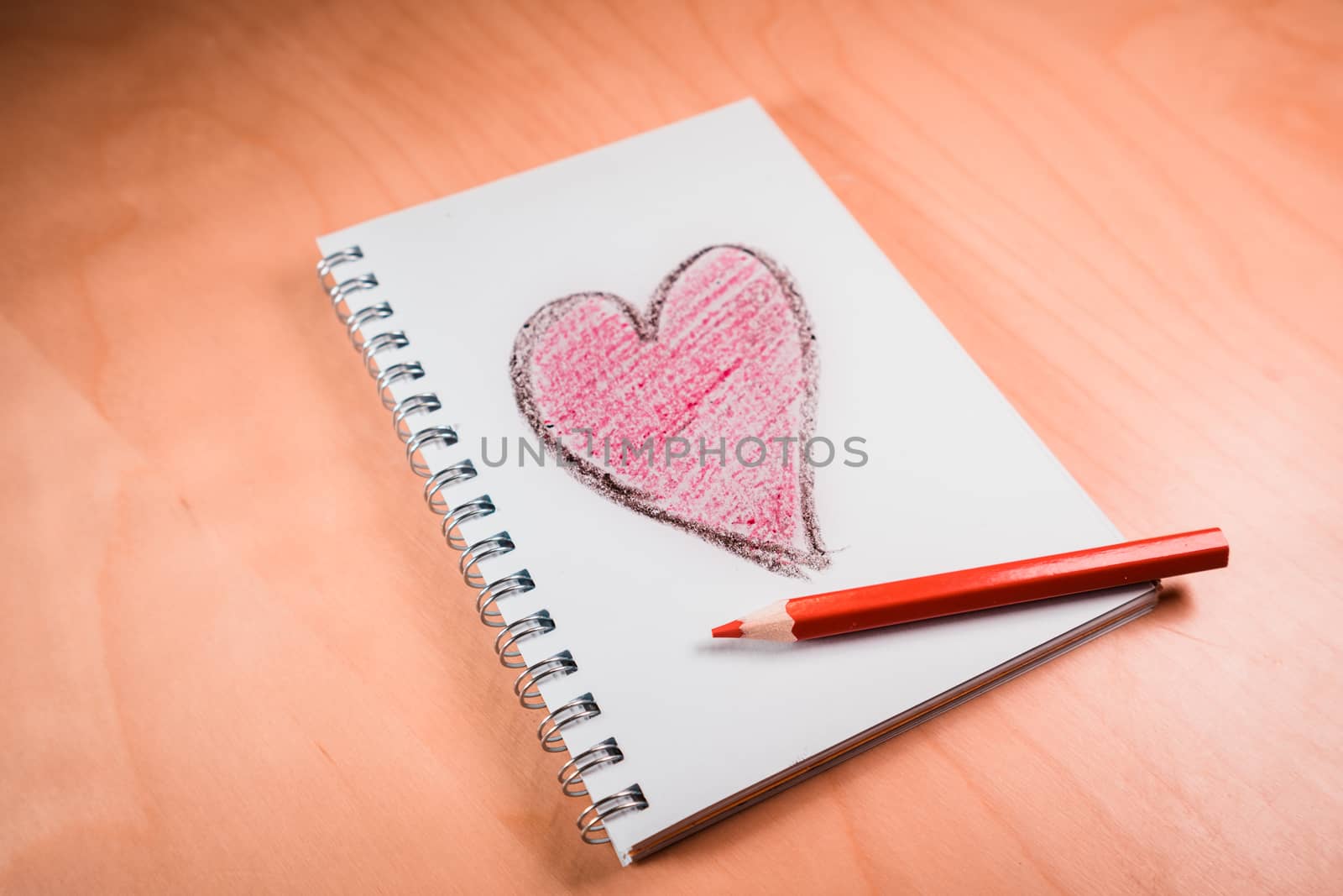 love heart on notebook with red pen on orange wooden table. Suitable for love, valentine, anniversary, couple and friendship concepts.