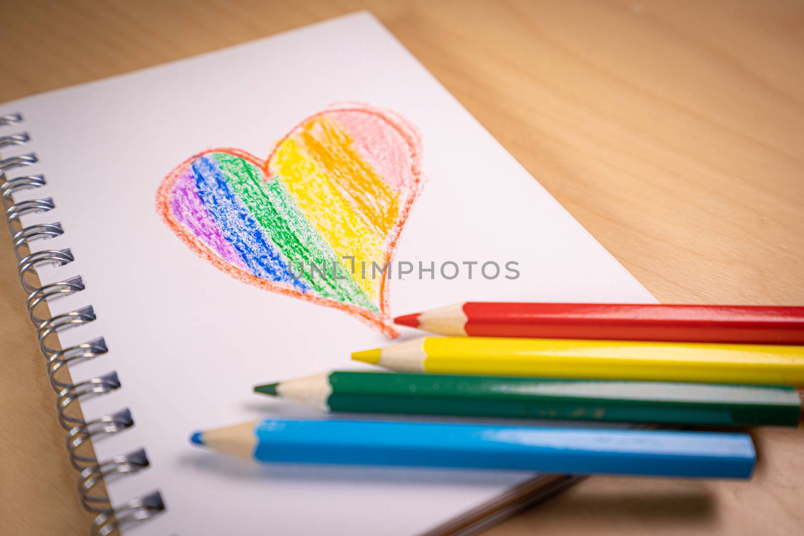 Heart with the colors of the LGTBI or GLBT flag on a blank notebook with rainbow pens by tanaonte