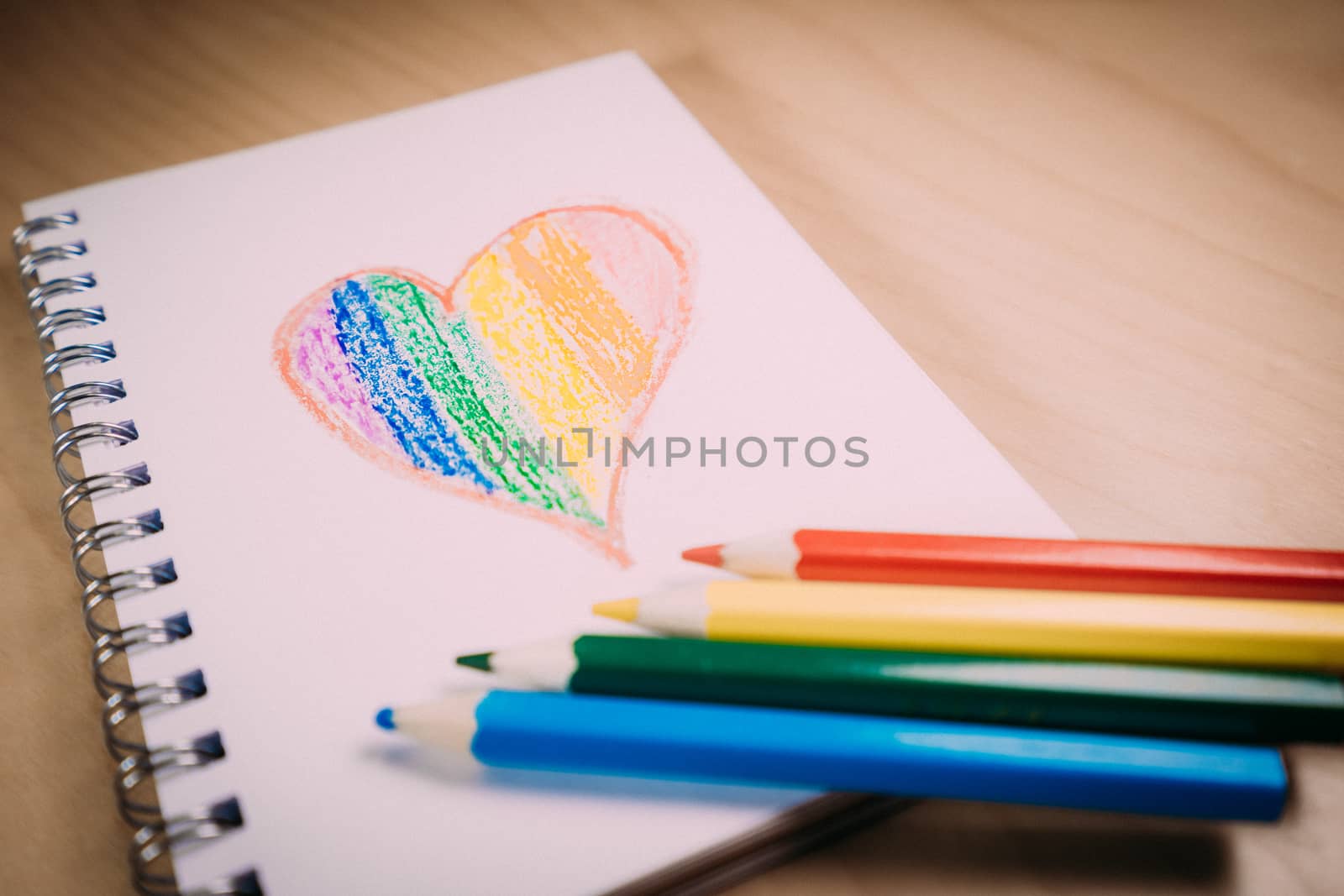 Heart with the colors of the LGTBI or GLBT flag on a blank notebook with rainbow pens by tanaonte