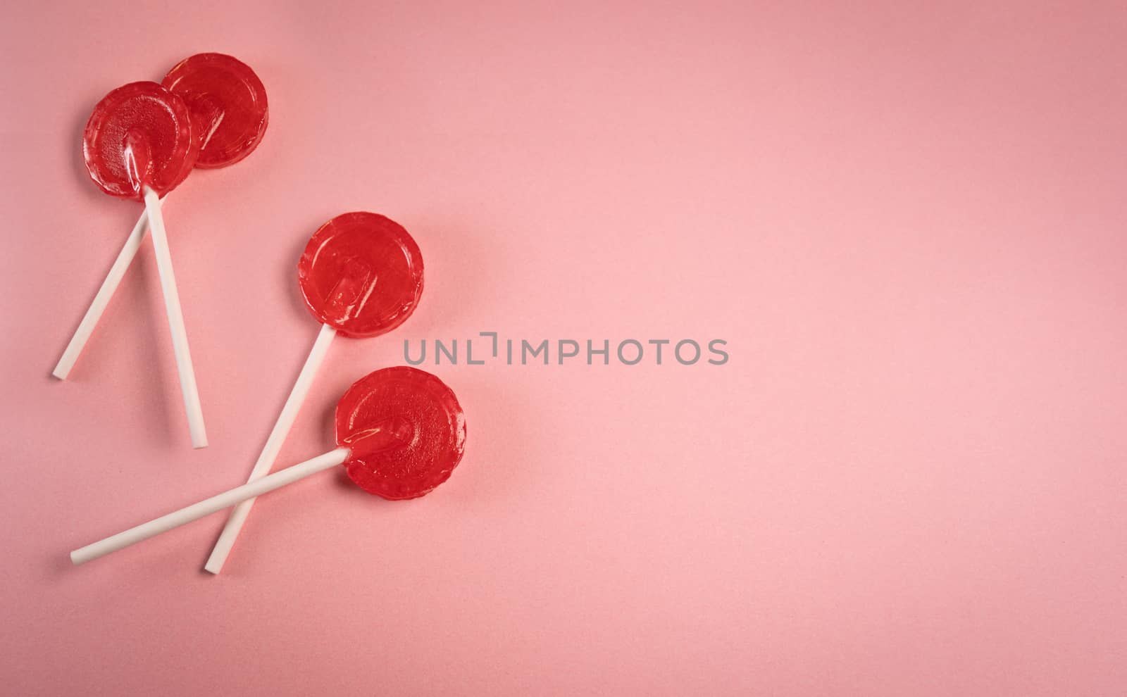 Round shaped red sweet tasty lollipops on pink pastel background. Copy space by tanaonte