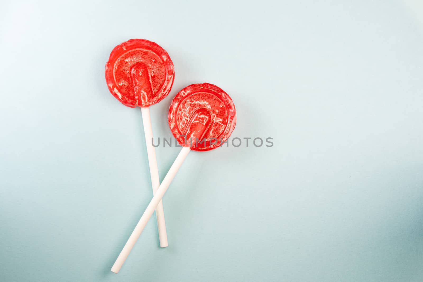 Round shaped red sweet tasty lollipops on blue pastel background. St. Valentine's day. Copy space.