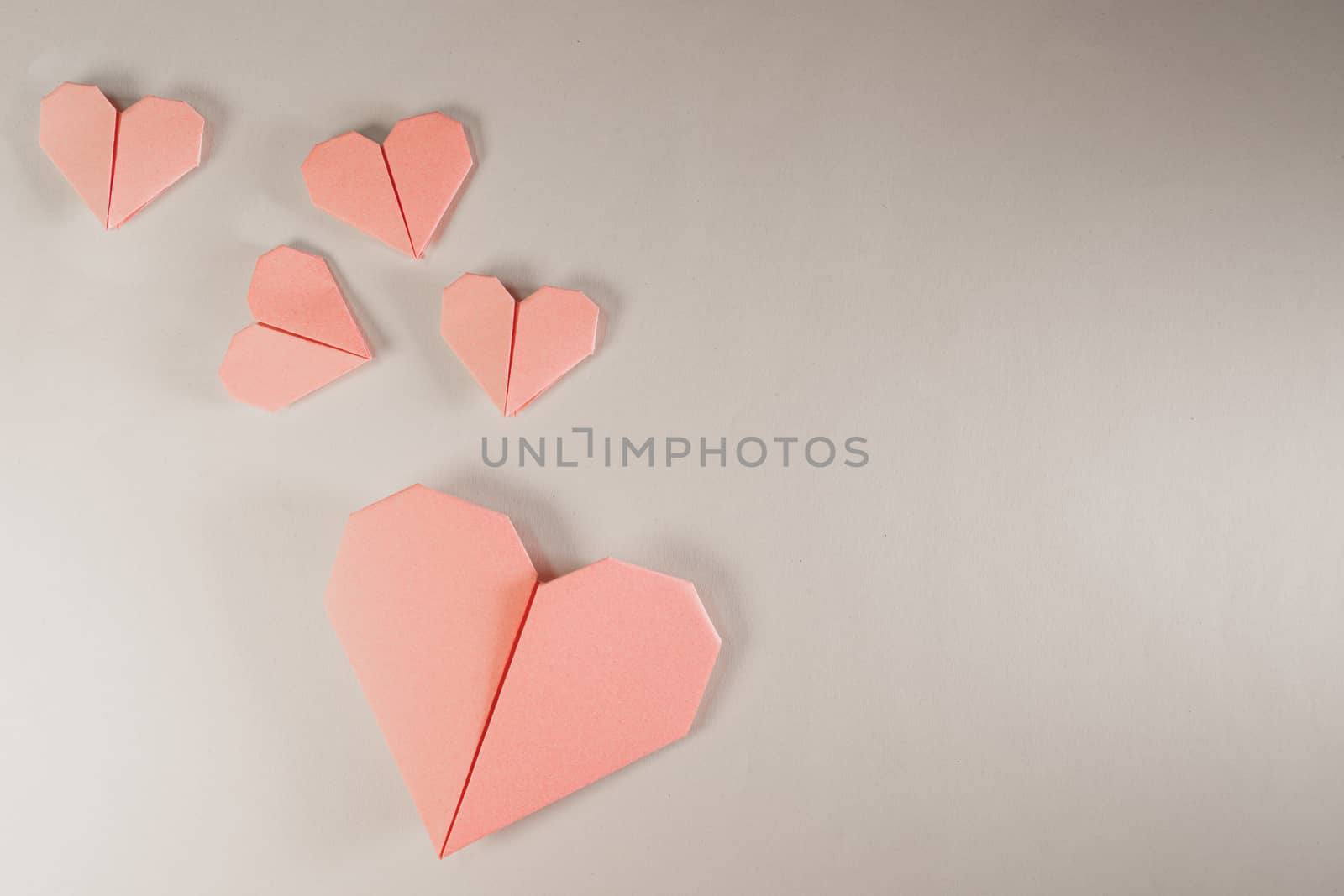 Pink origami hearts on a paper background. Paper craft, suitable for love, Valentine Day, romance and wedding concepts with copy space available.