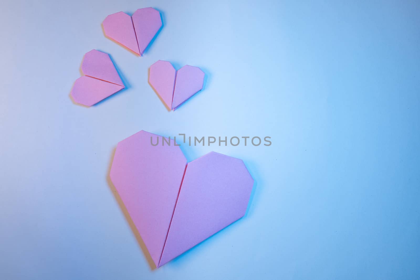 Pink origami hearts on a blue background. Paper craft, suitable for love, Valentine Day, romance and wedding concepts with copy space available.