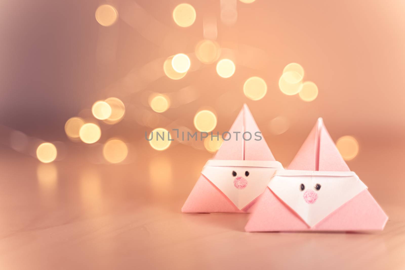 Origami Xmas scene with two pink Santa claus in paper craft and bokeh lights on the background. Sepia tone