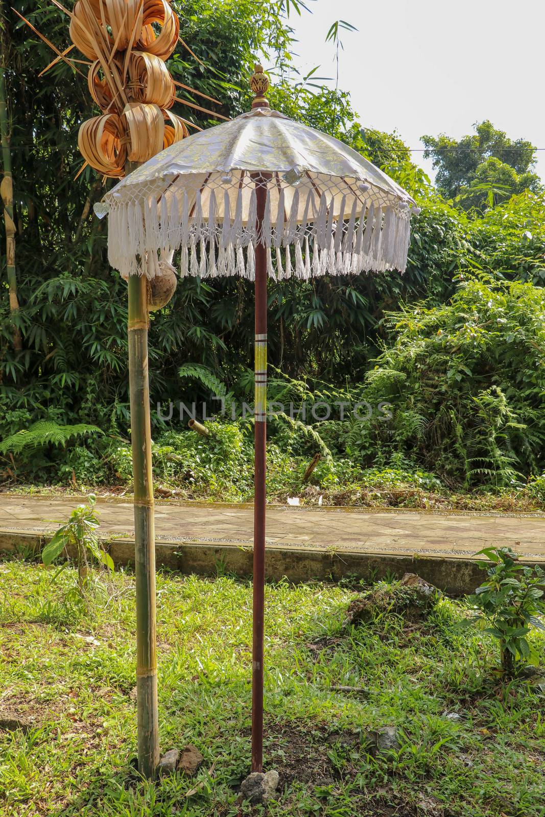 Decoration of Hindu temple complex Batukaru on Bali island in Indonesia. Yellow and white decorative umbrellas line the path for believing visitors. Colorful fabric umbrellas with decorative fringes.