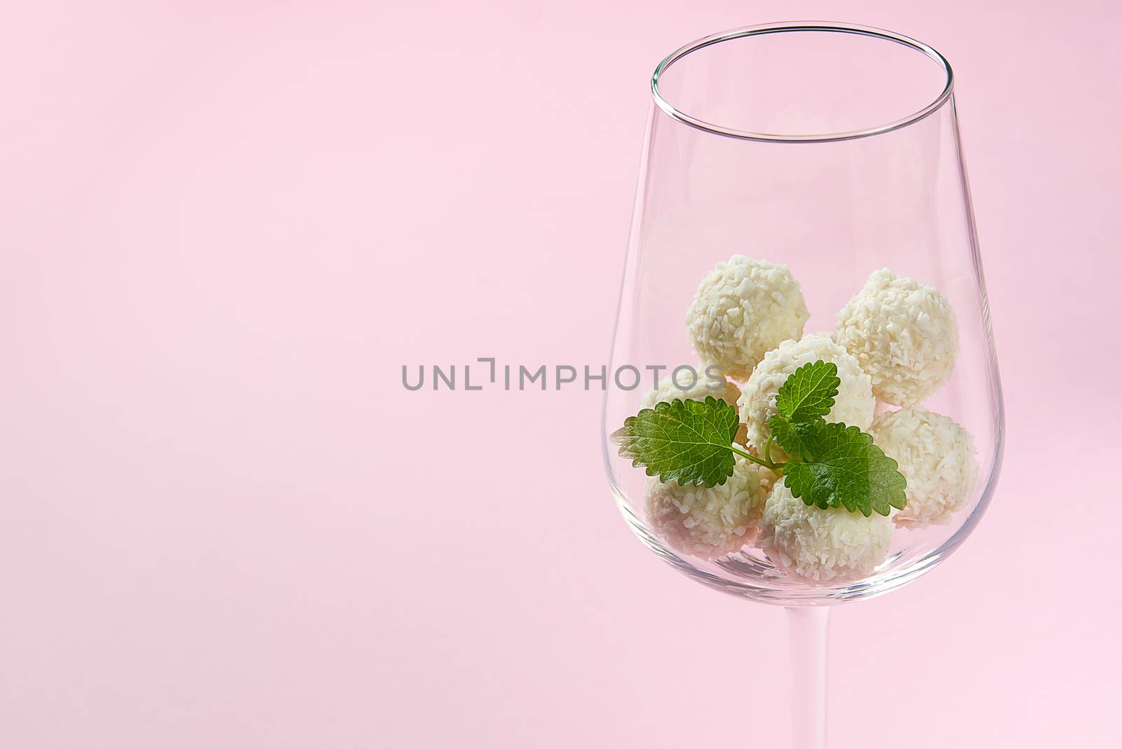 White Coconut Truffles in wine glass with mint leave. wine glass with Coconut cookies on pink background with copy space