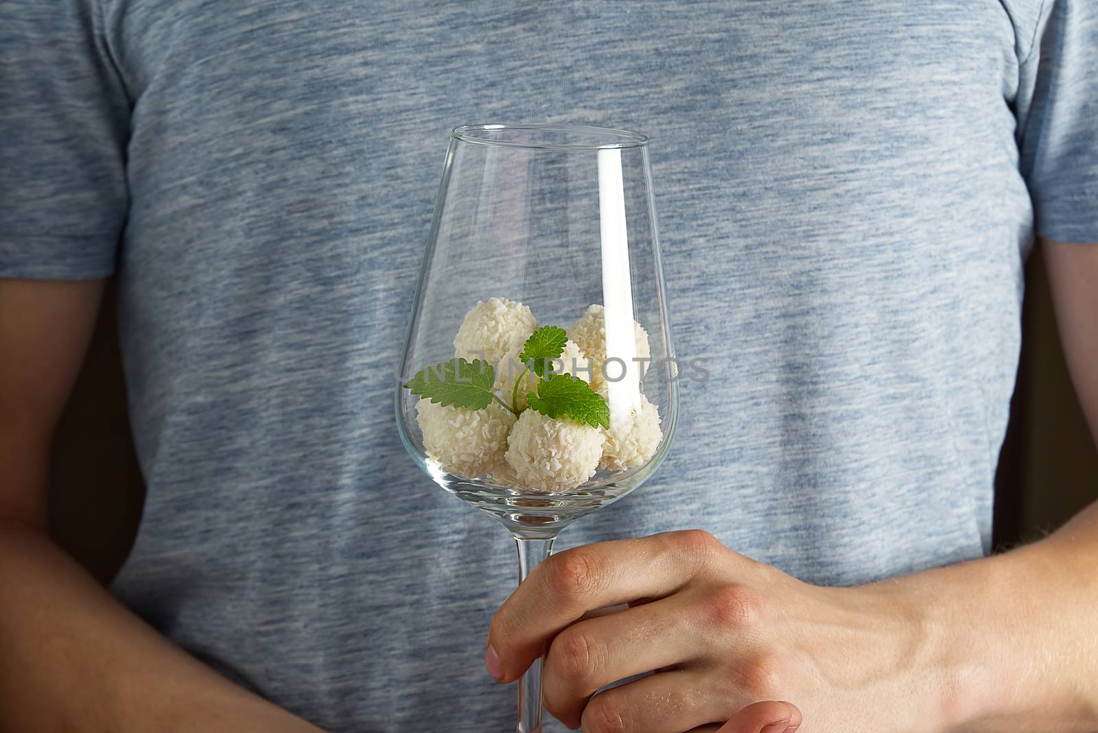 White Coconut Truffles in wine glass with mint leave. Man holding wine glass with Coconut cookies