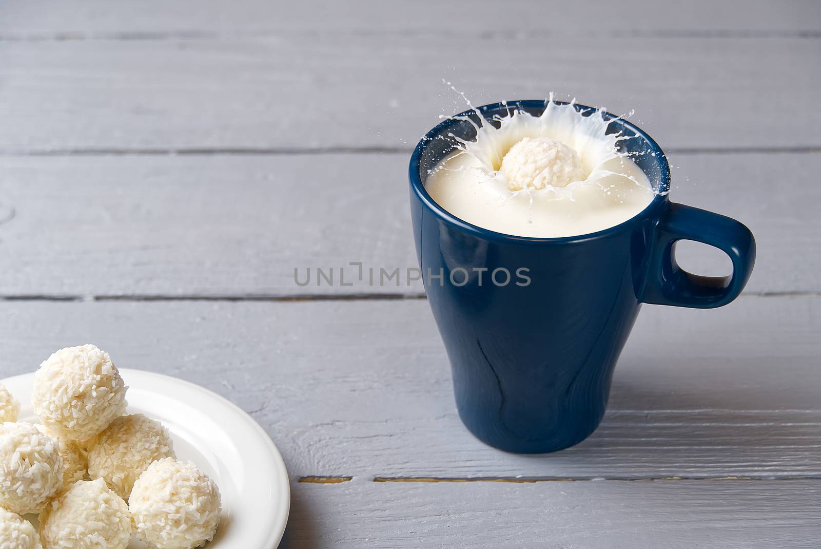 coconut cookies fell into a blue mug of milk. splashes of milk in a mug caused by a drop of coconut truffle. by PhotoTime