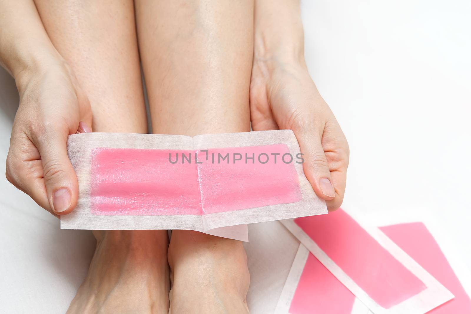 Beautiful woman doing depilation for her legs with waxing, isolated on white. Woman using pink wax strips.