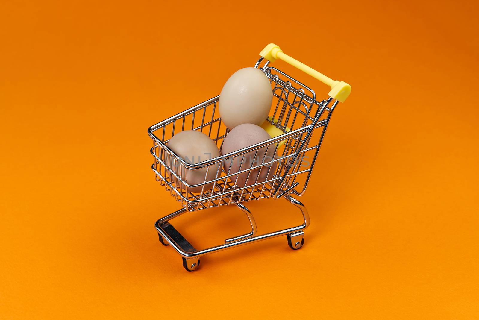 chicken eggs in a shopping cart. isolated on orange.