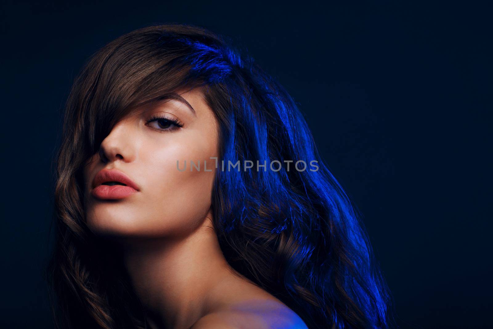 Portrait of beautiful brunette woman with hairstyle with bangs in studio with blue light