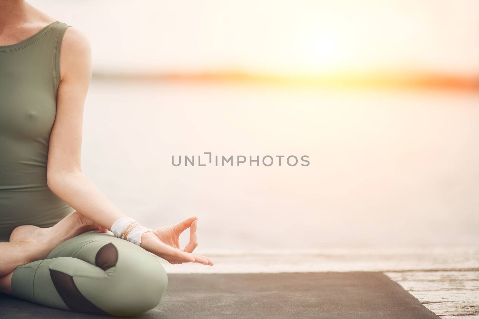 Yoga symbol. Lotus pose at the lake on sunset. Stylish modern woman.