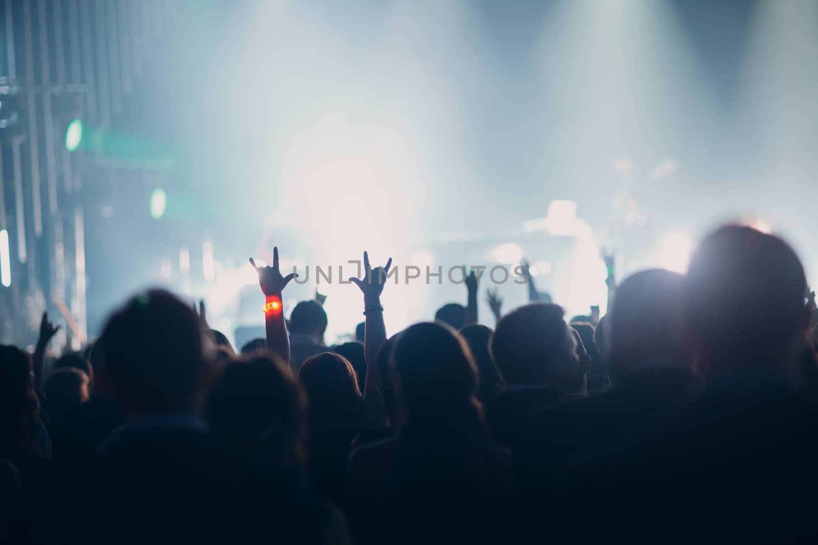 Concert, event or party concept. People with hands up at the scene, spotlight, colored blue light.