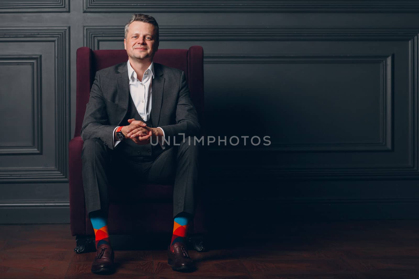 Portrait of smiling senior middle adult man in gray suit and colorful multi colored socks looking at camera with copy space.