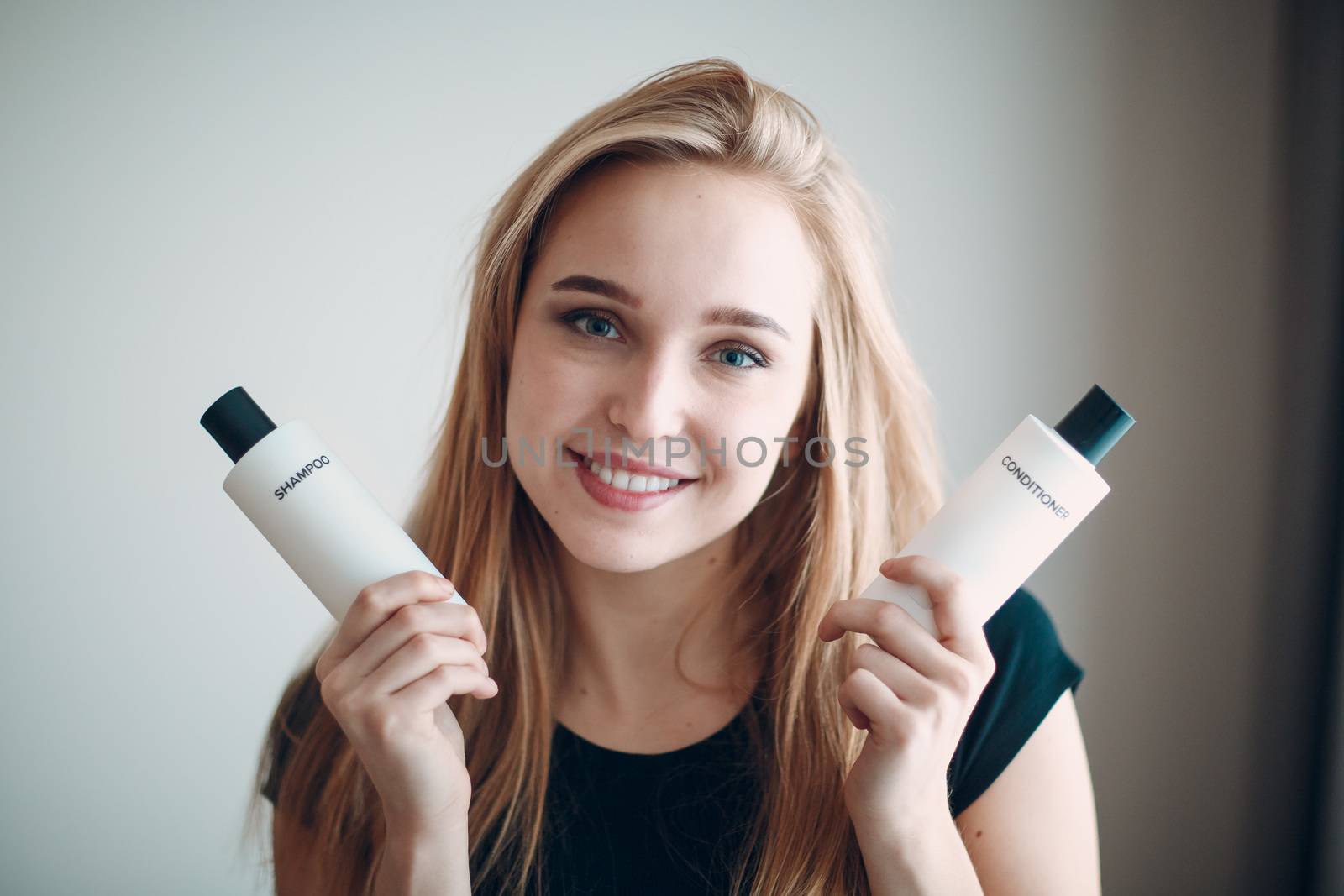 Pretty young woman hold two bottle with empty space. Shampoo and conditioner.