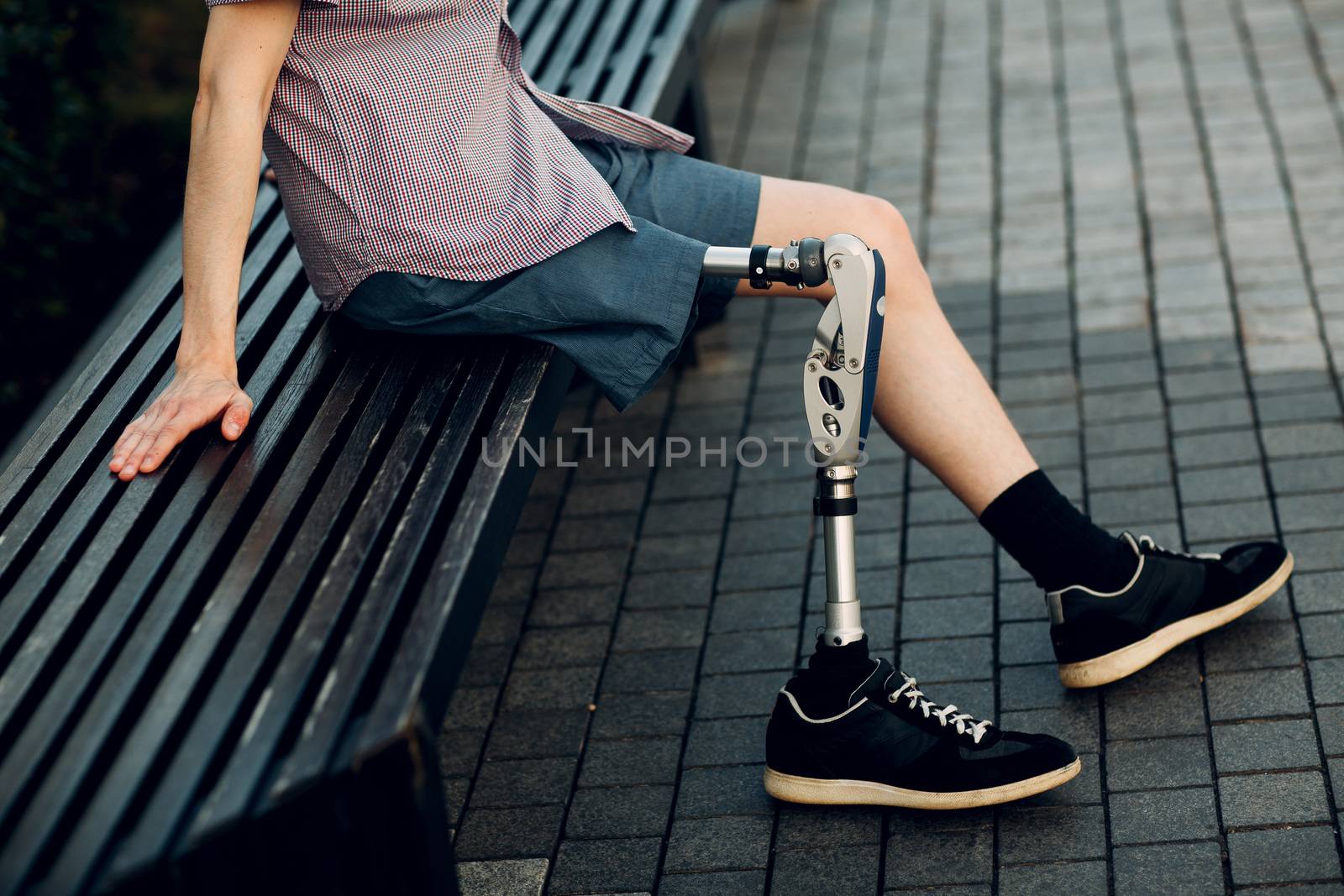 Disabled young man with foot prosthesis sitting outdoor by primipil