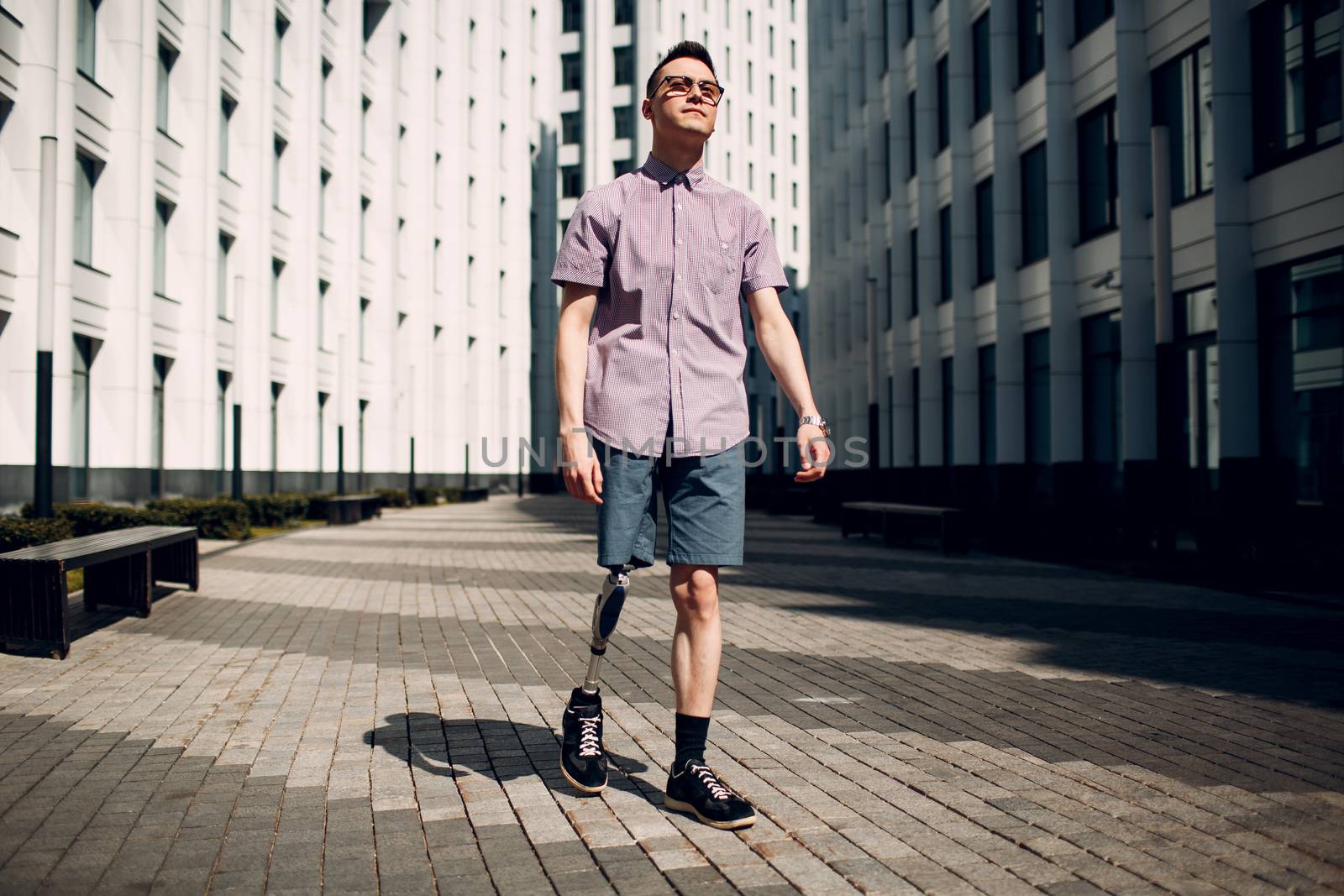 Disabled young man with foot prosthesis walks along the street. by primipil