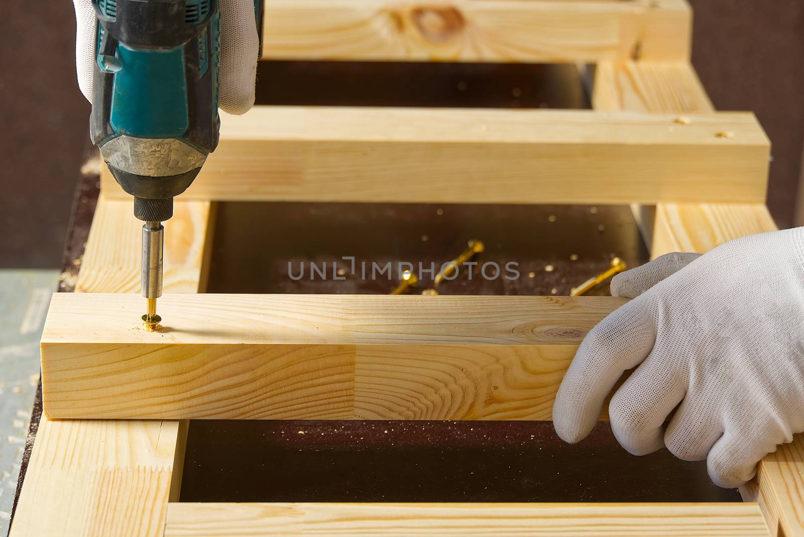 Carpenter, a man works with a cordless screwdriver. Drills and tightens the screws with a cordless drill. Working with wood in the carpentry workshop