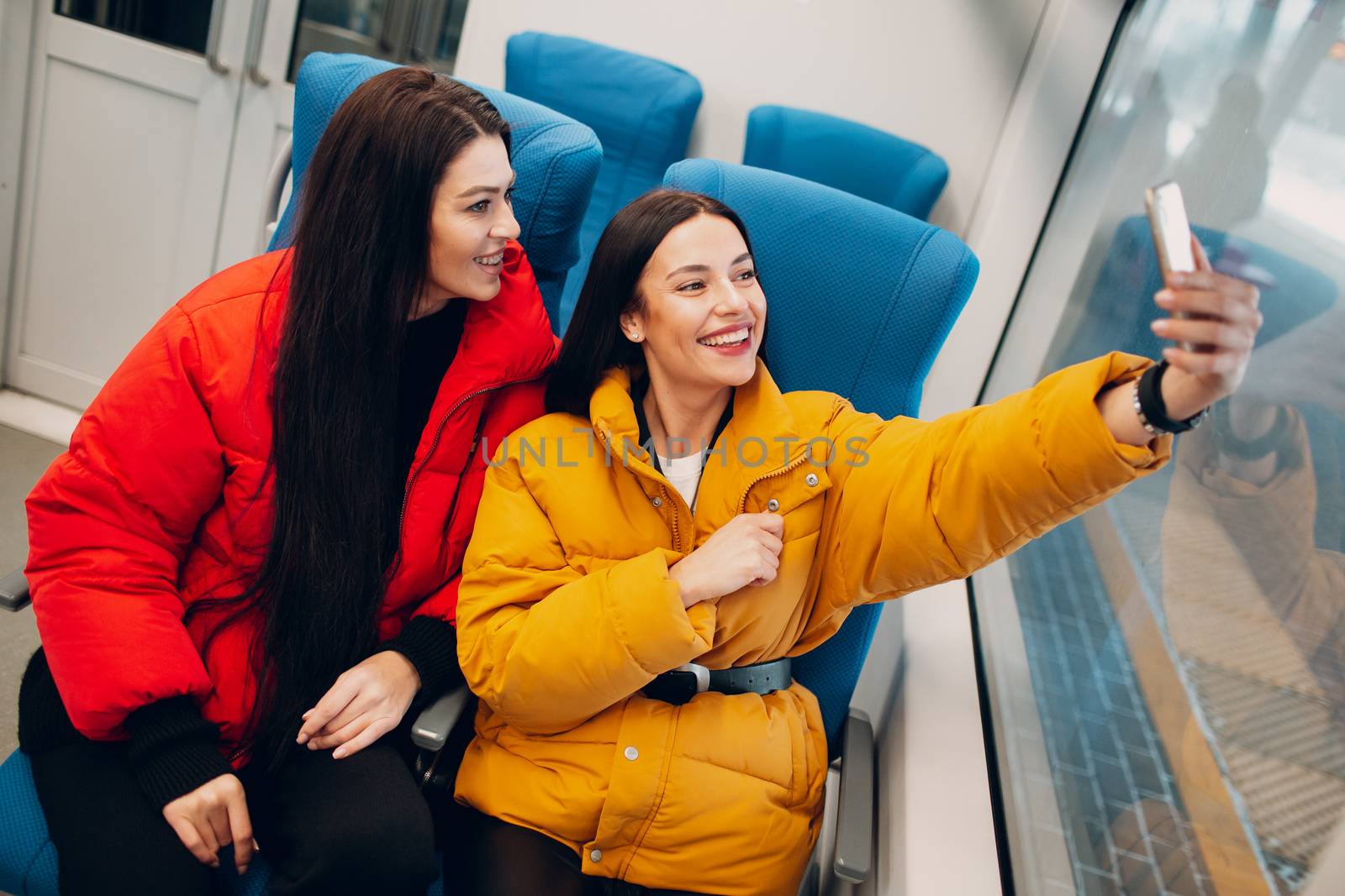 Two young women take a selfy shot with mobile phone in train by primipil