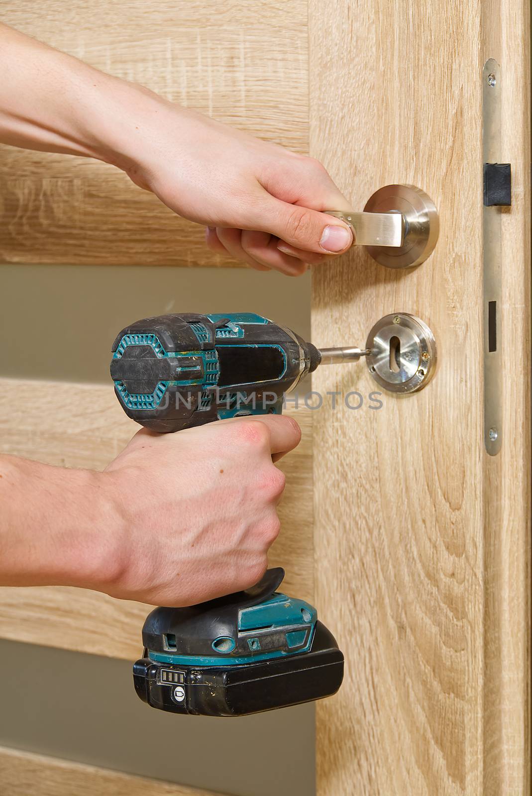 handyman repair the door lock in the room. man repairing the door handle furniture. carpenter at lock installation with electric drill into interior wood door by PhotoTime