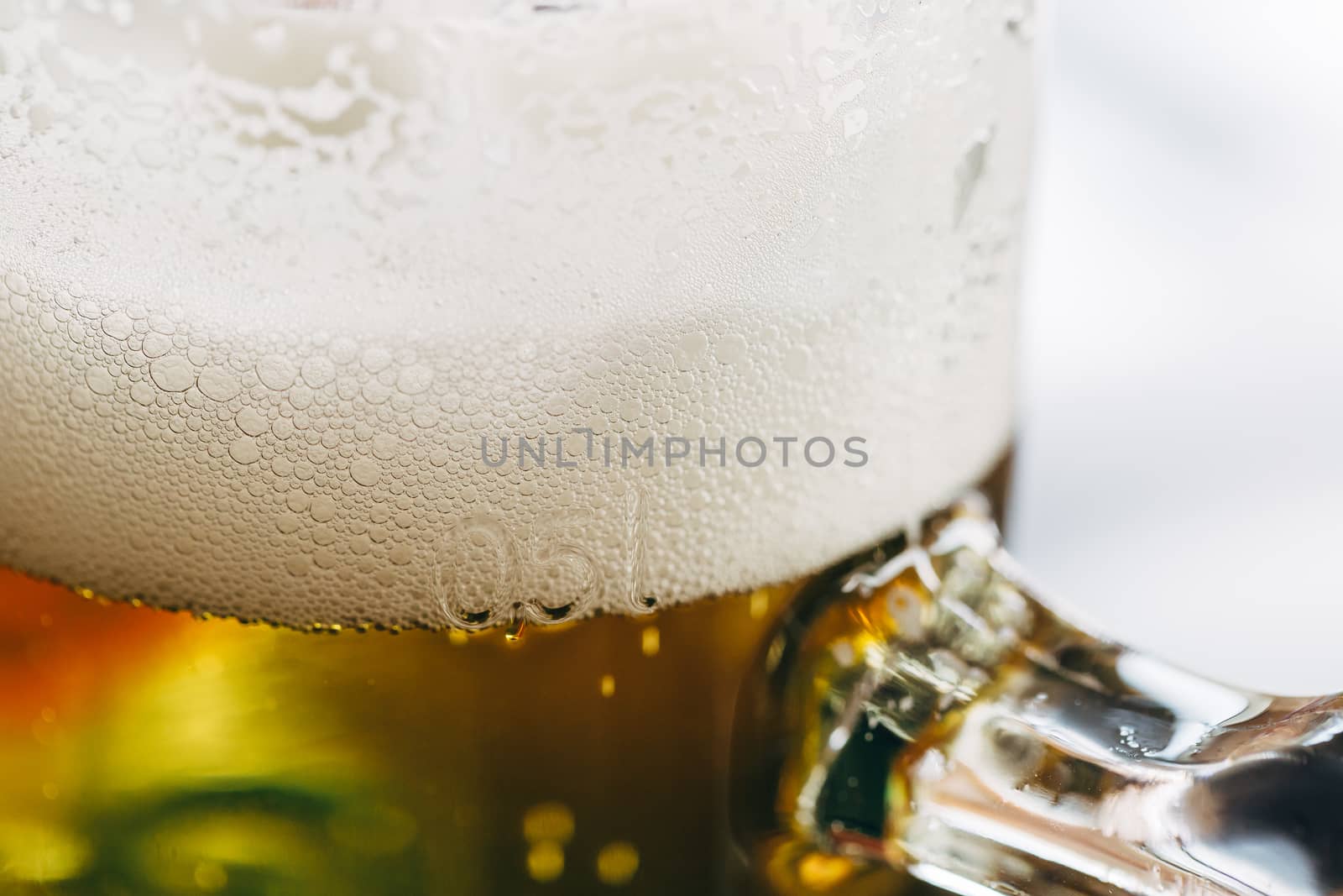 Close up of a half-liter glass of beer with frothy foam on top.