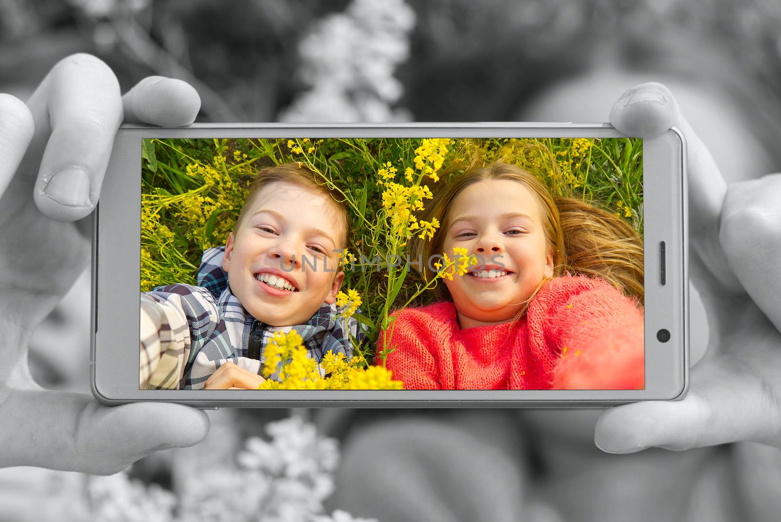Happy smiling kids making self portrait on smartphone in meadow. young boy and girl making selfie on smartphone laying in green grass with yellow flowers. by PhotoTime