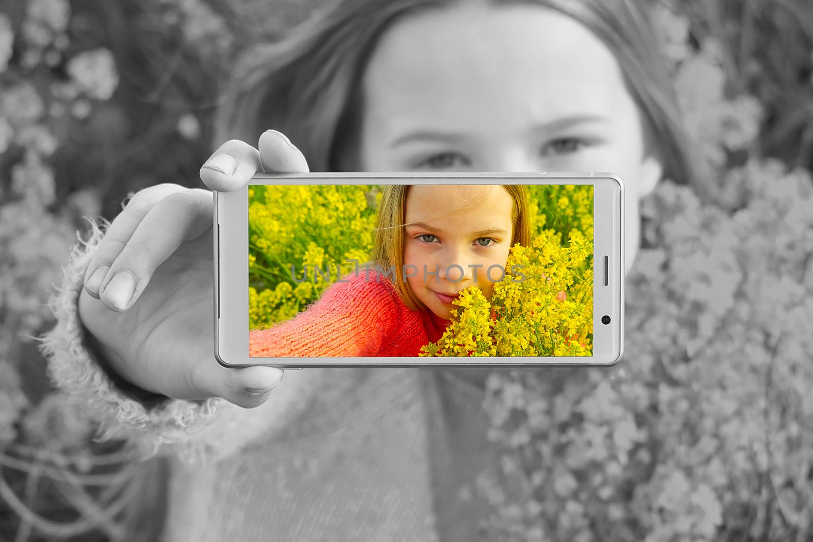 Happy smiling girl making self portrait on smartphone in meadow. young girl making selfie on smartphone laying in green grass with yellow flowers