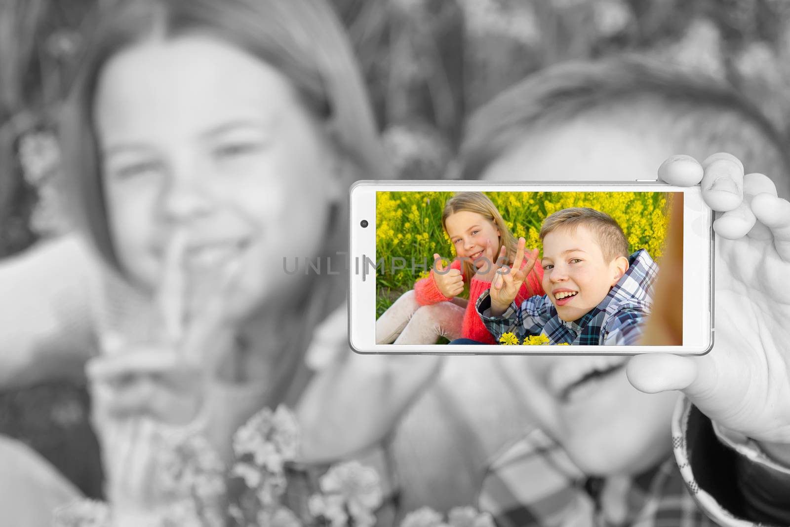 Happy smiling kids making self portrait on smartphone in meadow. young boy and girl making selfie on smartphone laying in green grass with yellow flowers