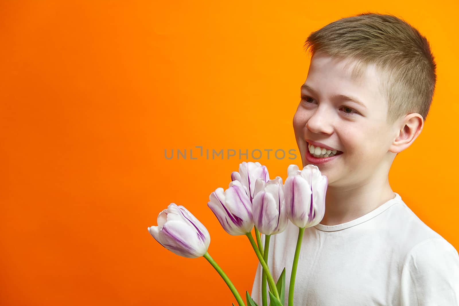 smiling young handsome boy on an orange background with tulips in hands. Children happiness. by PhotoTime