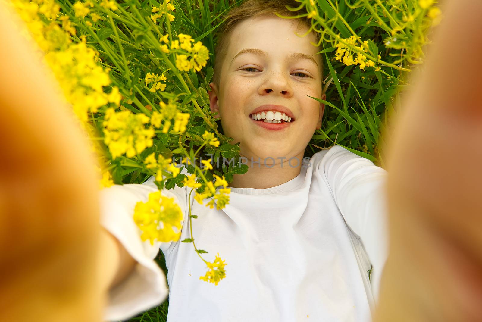 Happy smiling boy making self portrait on smartphone in meadow. young boy making selfie on smartphone laying in green grass with yellow flowers. by PhotoTime