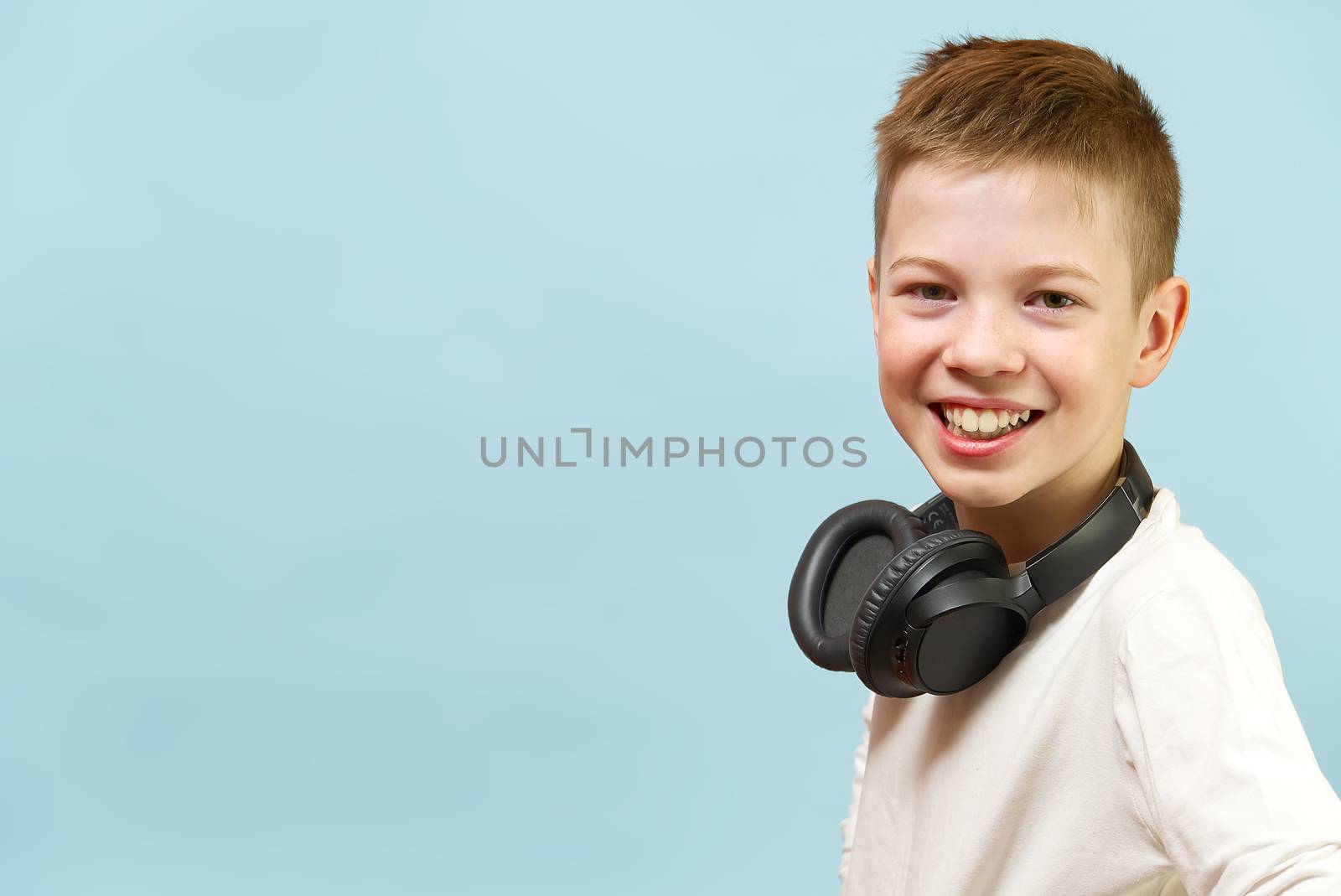 Smiling young handsome boy on a blue background in headphones. concept of baby radio, dj, singer or karaoke. happiness be music everywhere. by PhotoTime