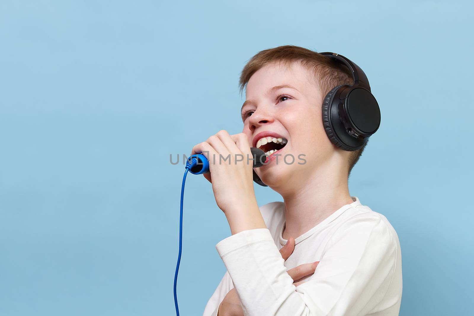 Smiling young handsome boy on a blue background in headphones. concept of baby radio, dj, singer or karaoke. happiness be music everywhere