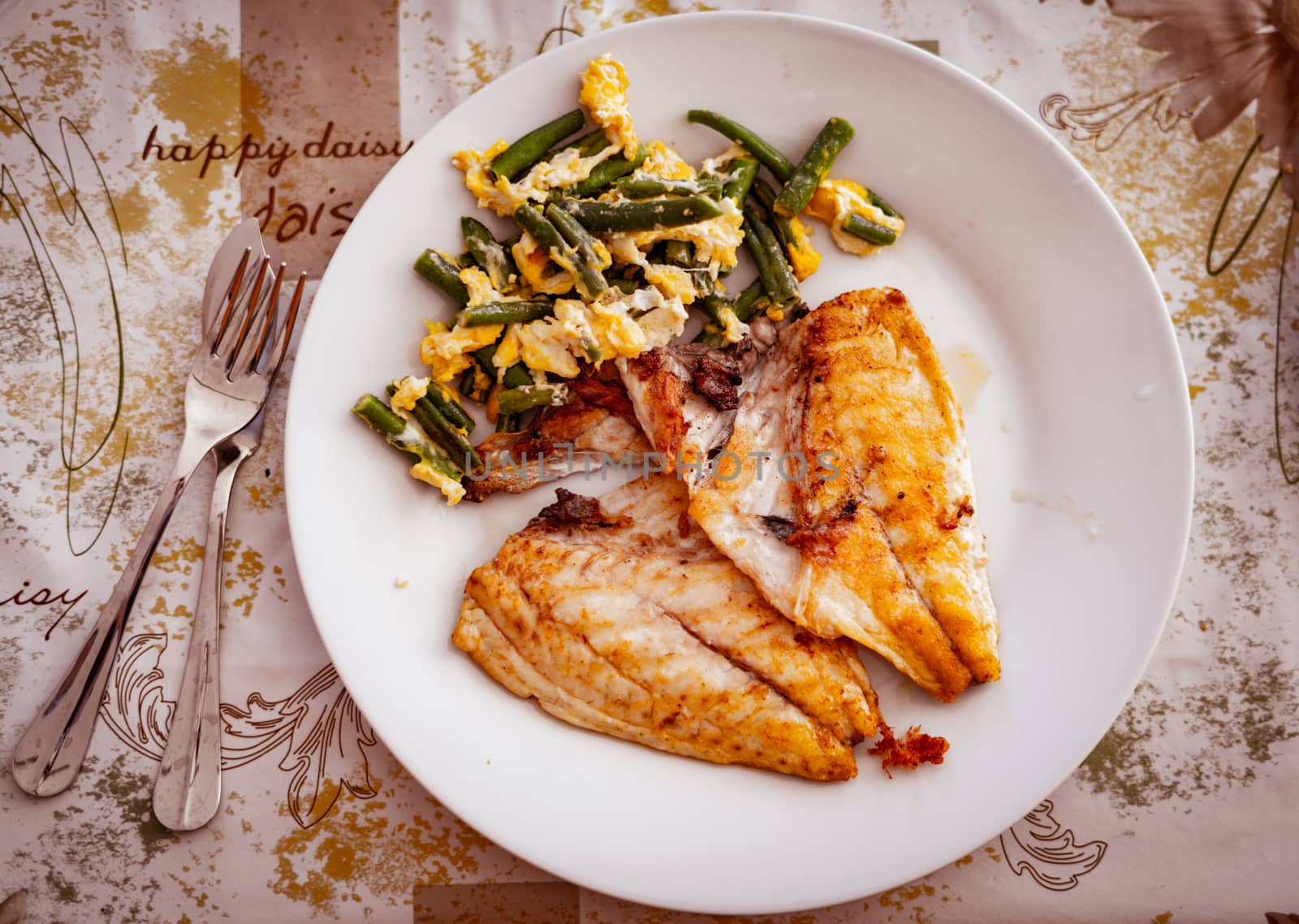 Grilled fish fillet and scrambled eggs and vegetables on plate, top view by tanaonte