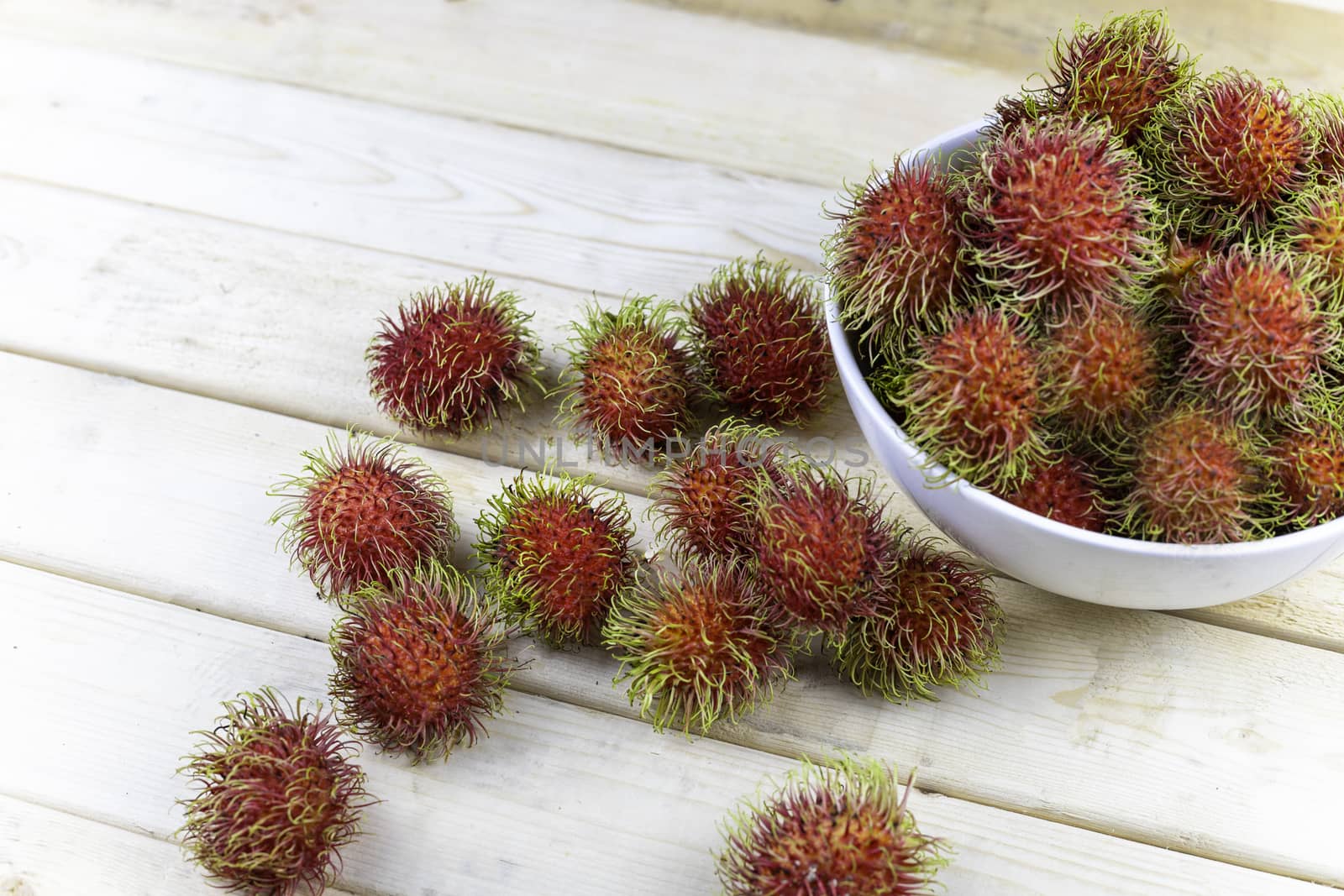 fresh rambutan in white blow and some drop on wood table.