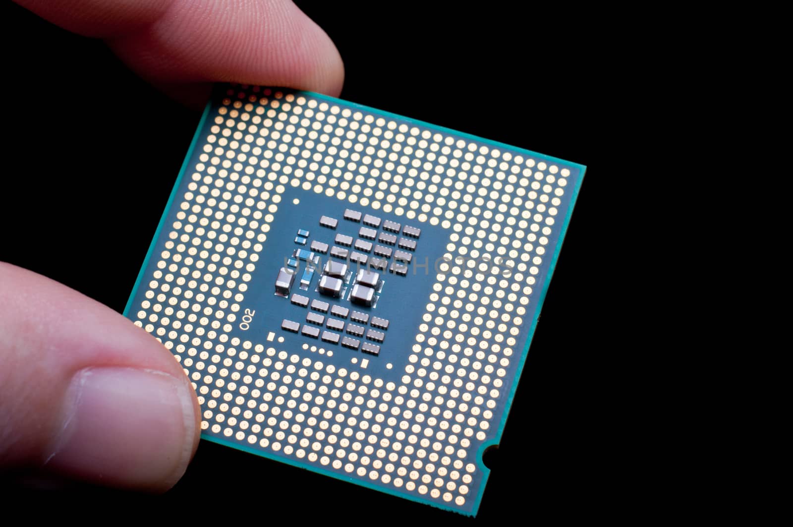 Close-up of a computer processor microchip held between the fingers and isolated on a black background