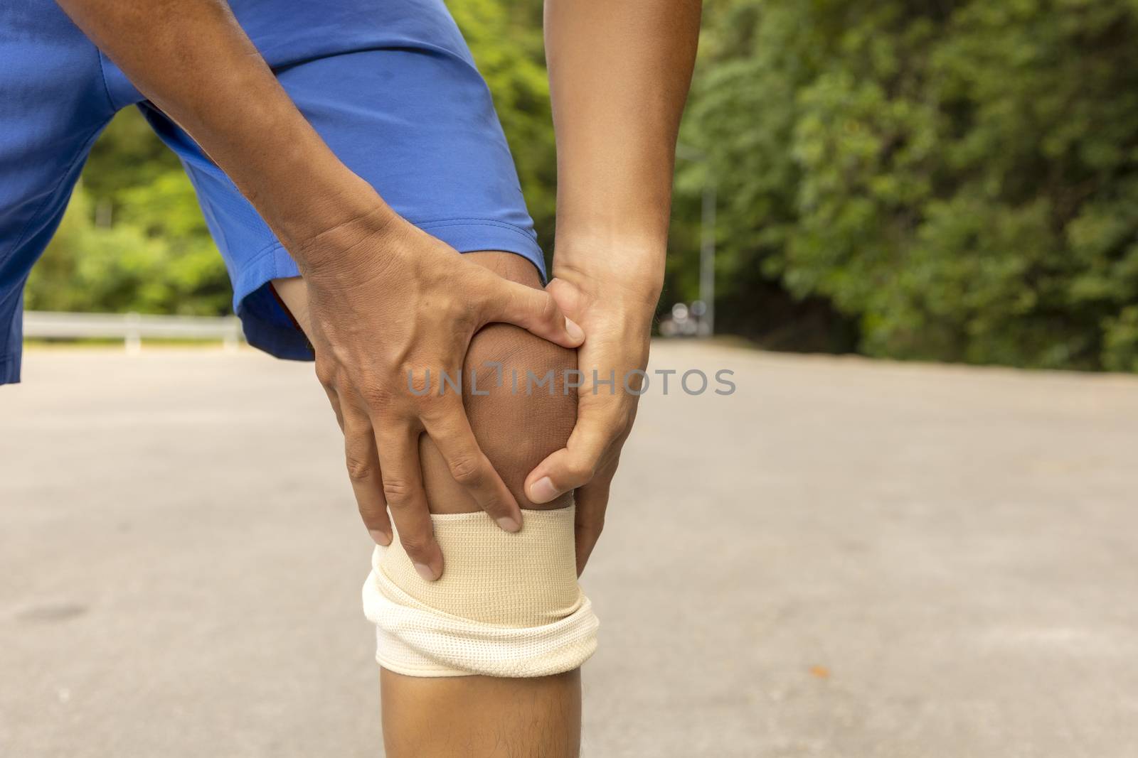 Man with blue runing shorts use hands hold on his knee after running on road in morning time with copy space for text or design
